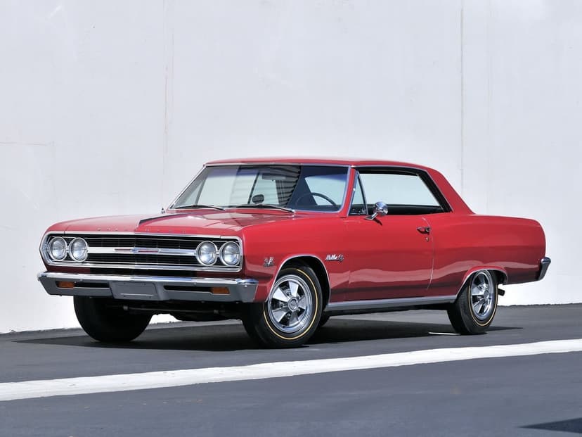 Red 1965 Chevrolet Chevelle Malibu SS classic muscle car with chrome trim on asphalt against a white wall.