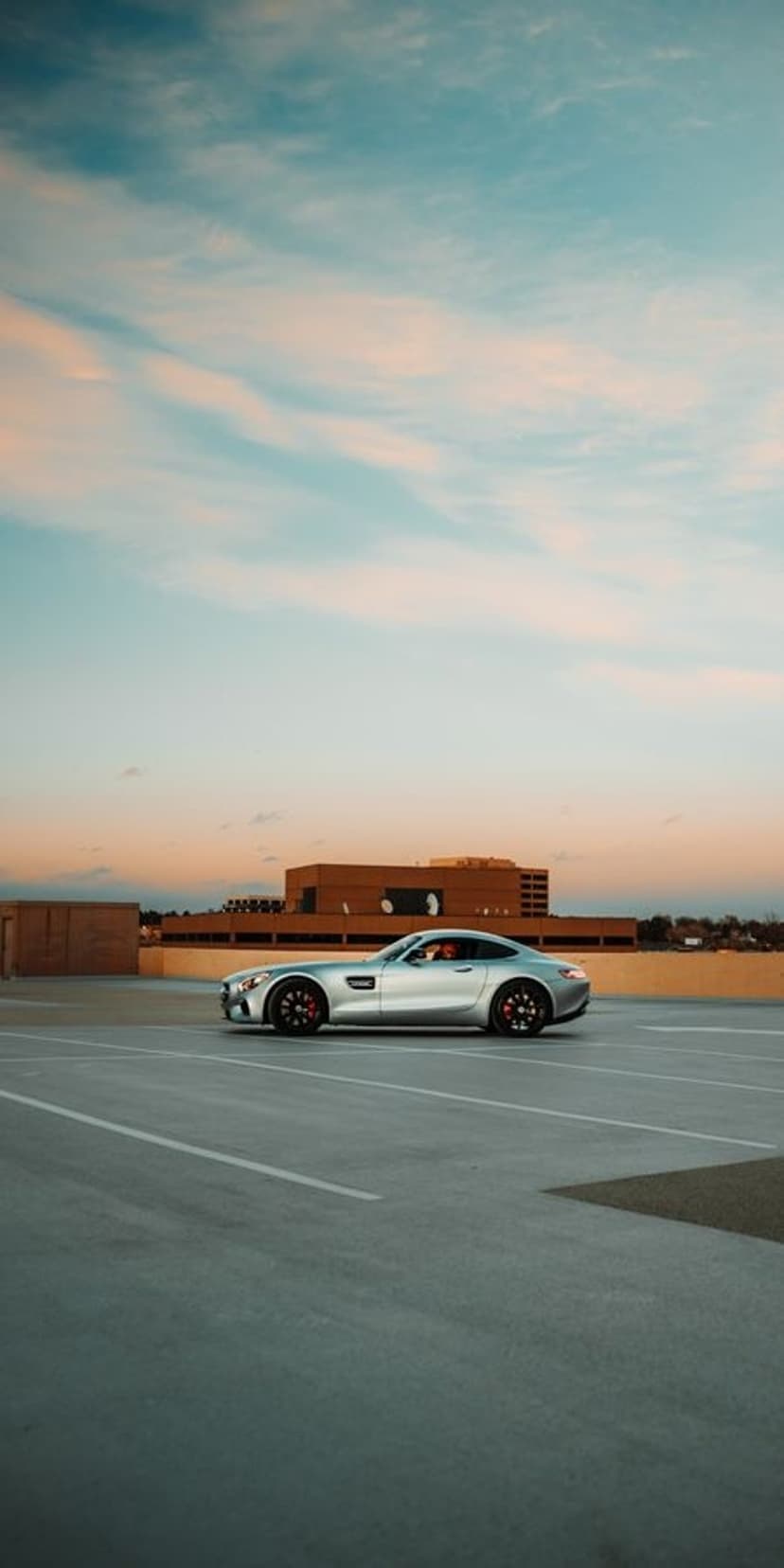 Silver Mercedes-AMG GT sports car parked on a concrete rooftop under a pink and blue gradient sunset sky.