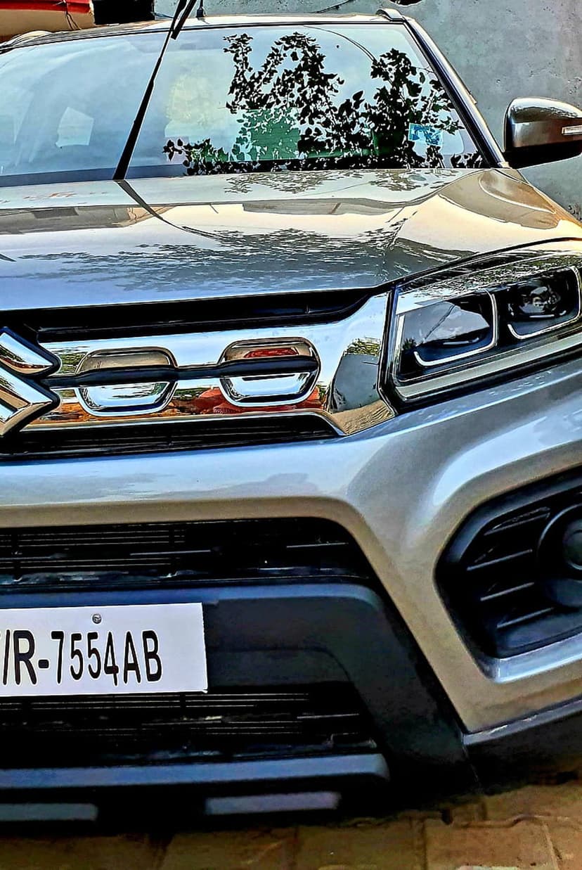 Maruti Suzuki Vitara Brezza front grille and chrome accents featuring sharp LED headlights on a silver vehicle.