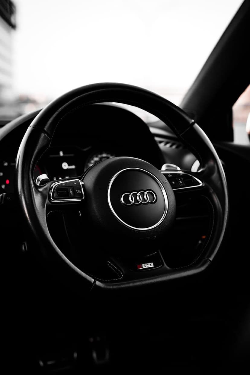 Audi steering wheel logo and black leather trim with integrated buttons in a dark luxury car interior.