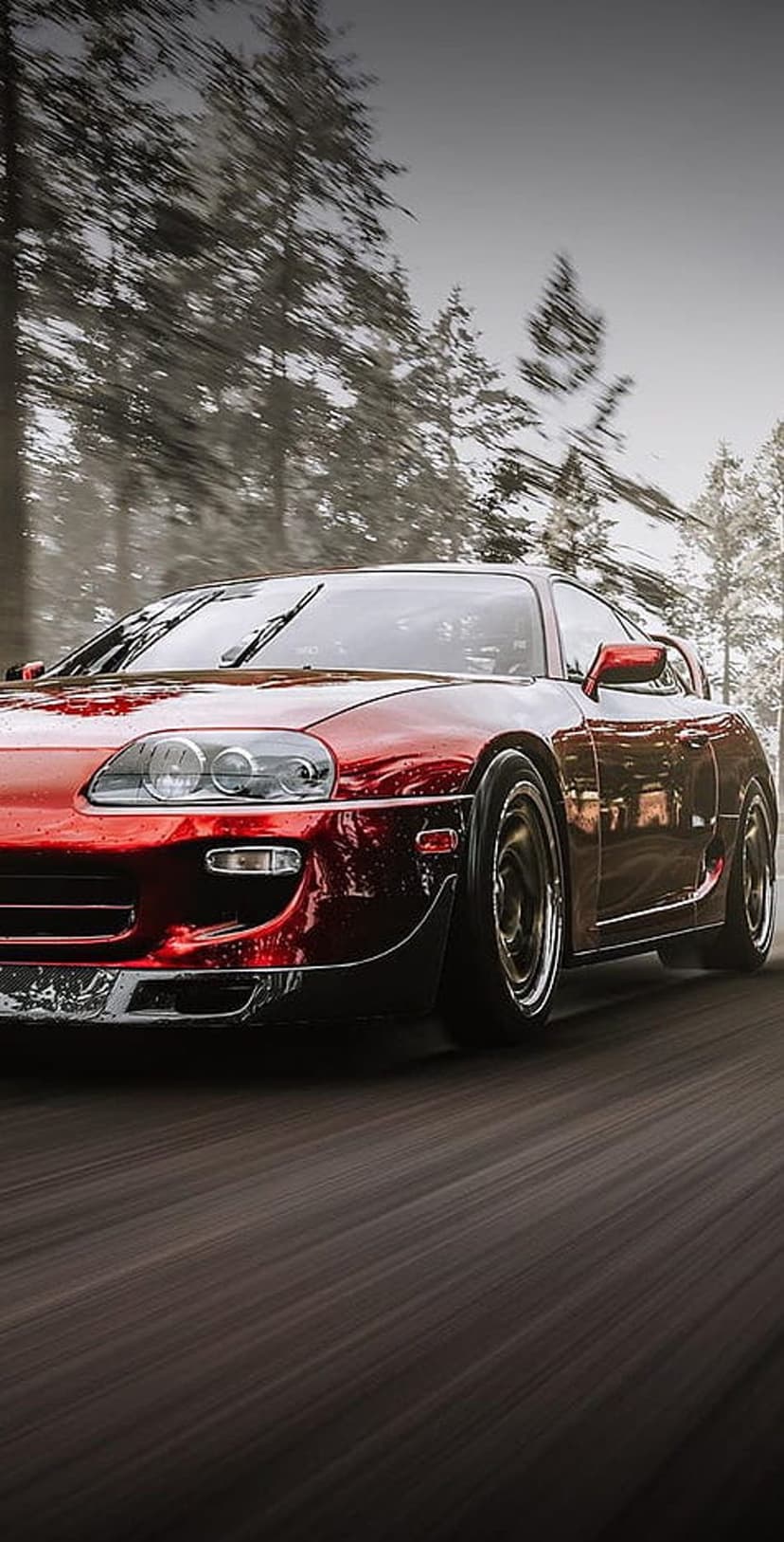 Red Toyota Supra sports car driving on a wet road through a foggy forest with tree reflections on the hood.