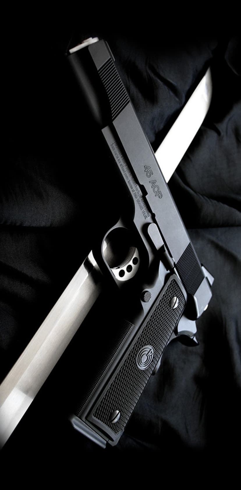 1911 semi-automatic pistol crossed over a metallic katana sword on a dark draped fabric backdrop with side lighting.