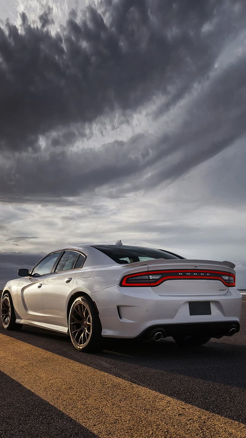 White Dodge Charger SRT Hellcat rear view on asphalt under dark storm clouds with glowing red taillights.