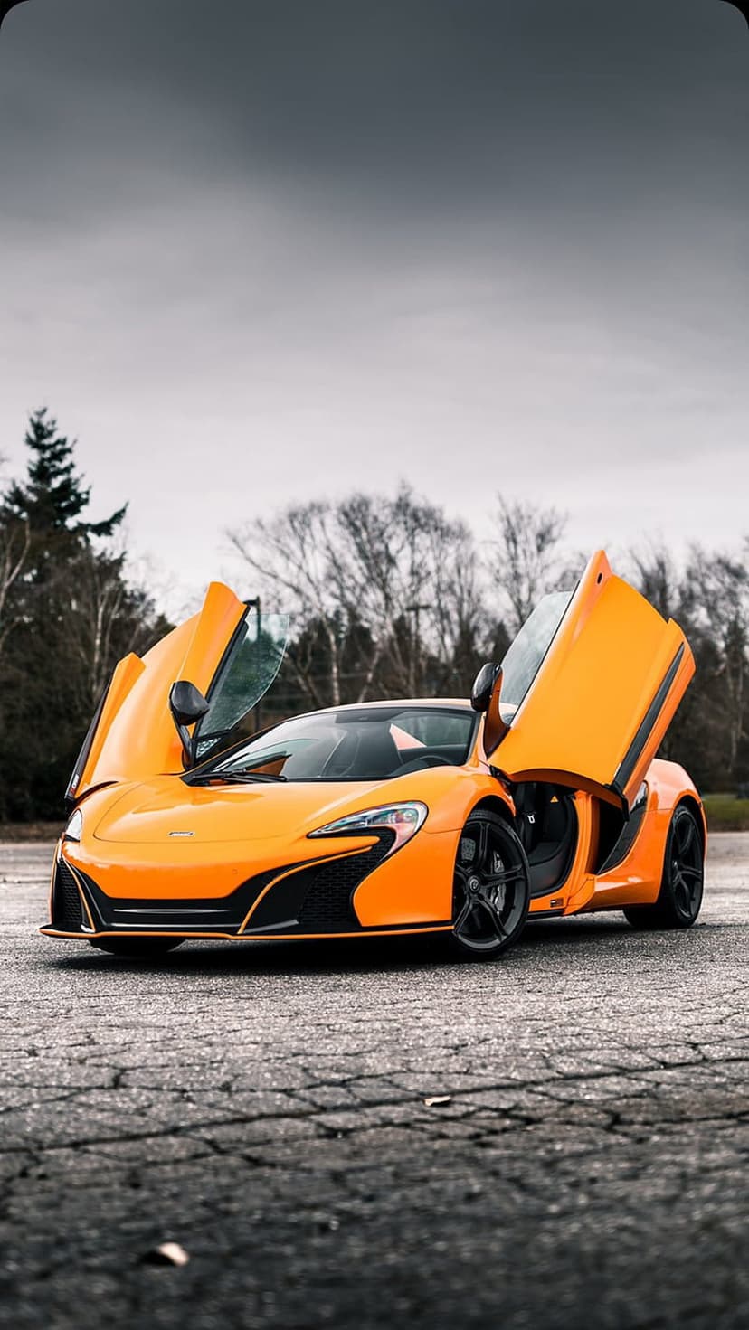 Orange McLaren supercar with open scissor doors parked on cracked asphalt under a gloomy, overcast grey sky.