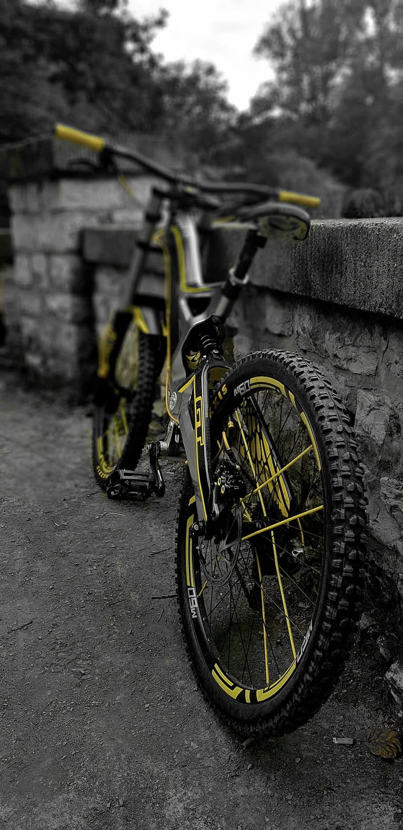 Yellow downhill mountain bike leaning on a gray stone wall with sharp focus on the front wheel and fork.