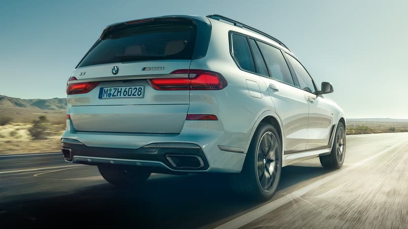 White BMW X7 M50i driving on a desert road at sunset with mountains and motion blur in the background.