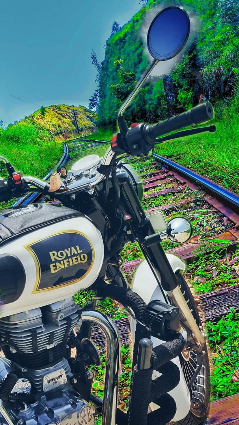 Royal Enfield motorcycle on rusty train tracks surrounded by lush green hills and a clear blue summer sky.