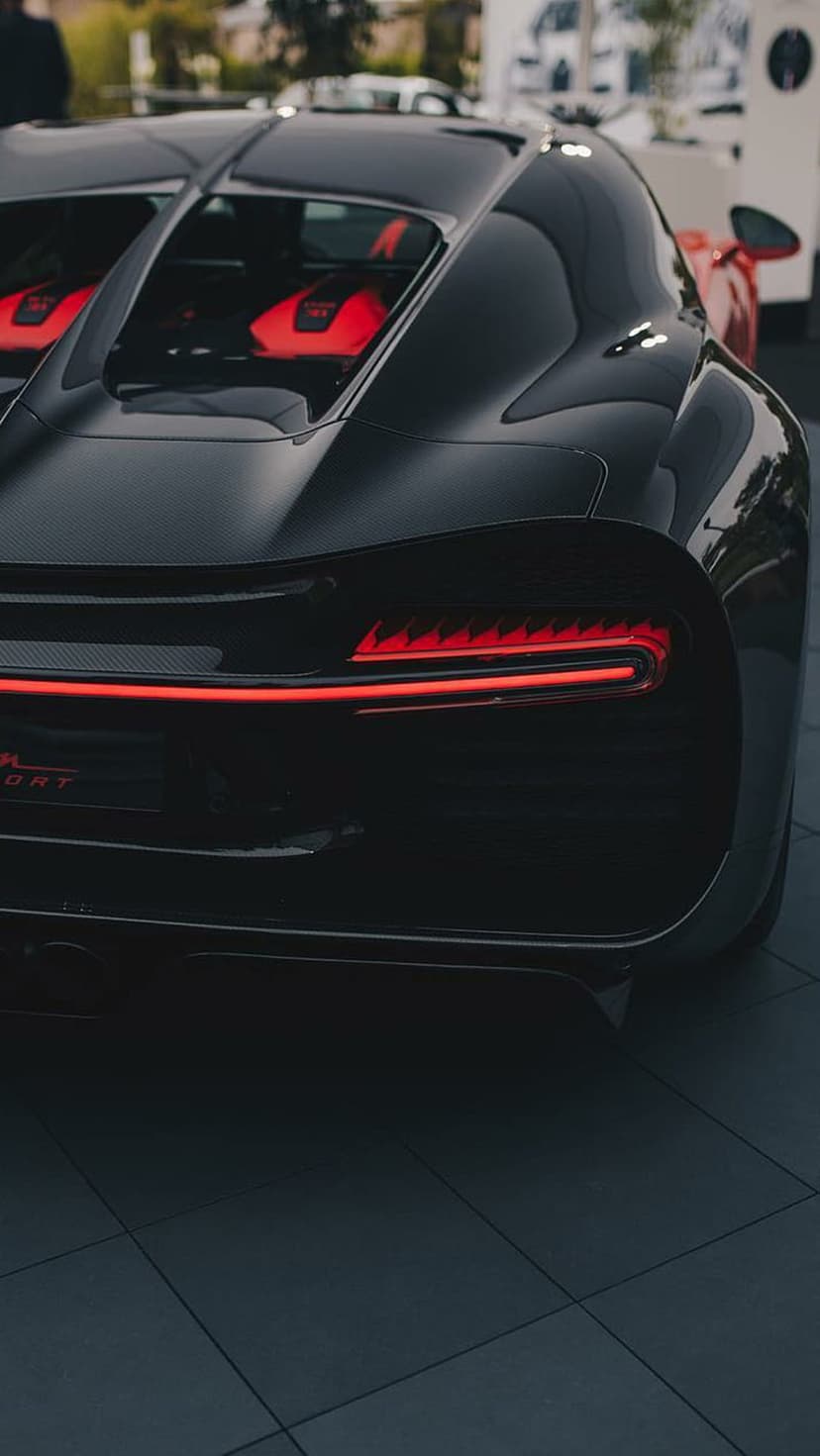 Bugatti Chiron Sport rear taillight glowing red against a black aerodynamic body with a glimpse of red interior.