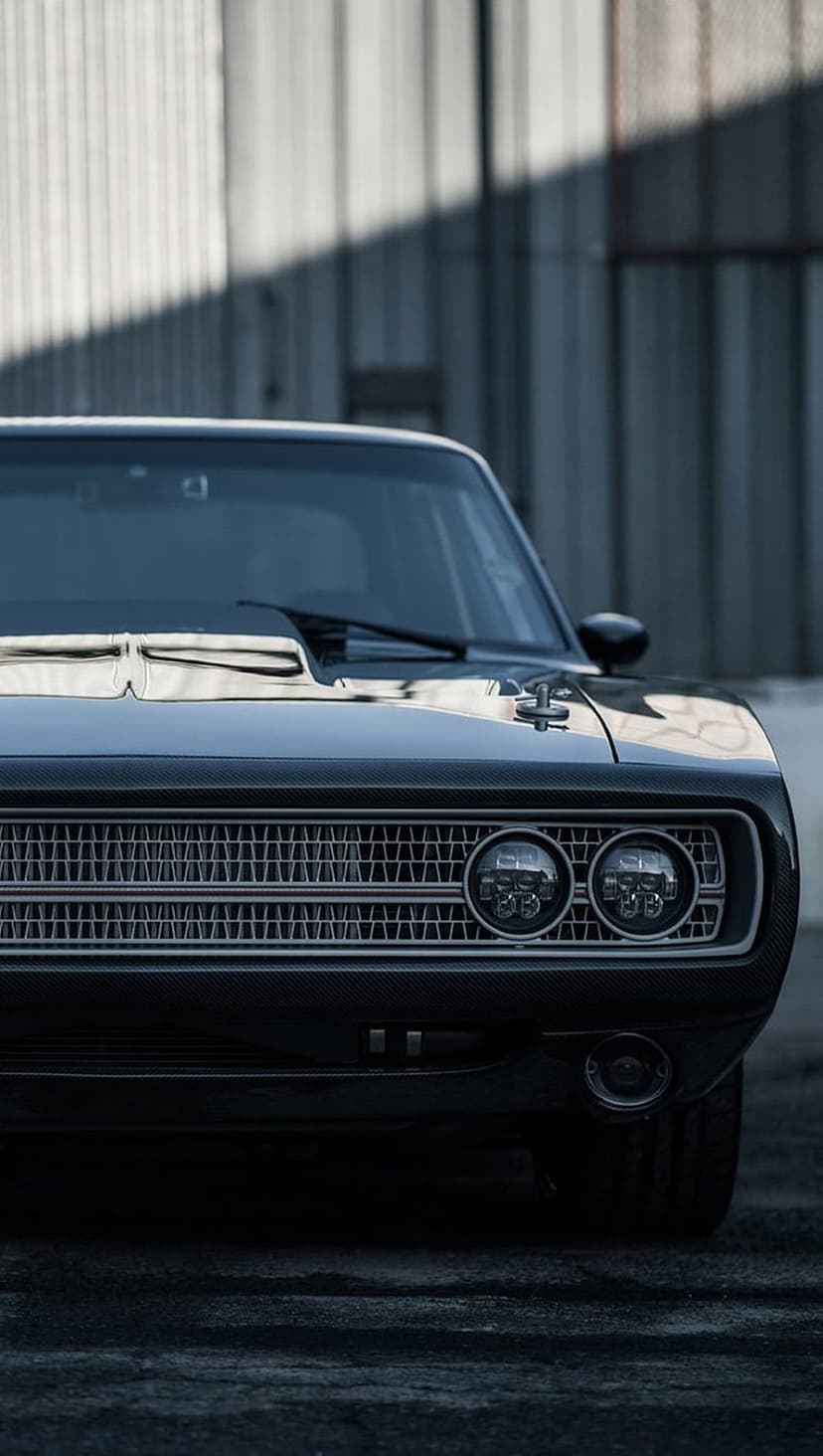 Black Dodge Charger front grille and dual round headlights illuminated against a dark, textured background.