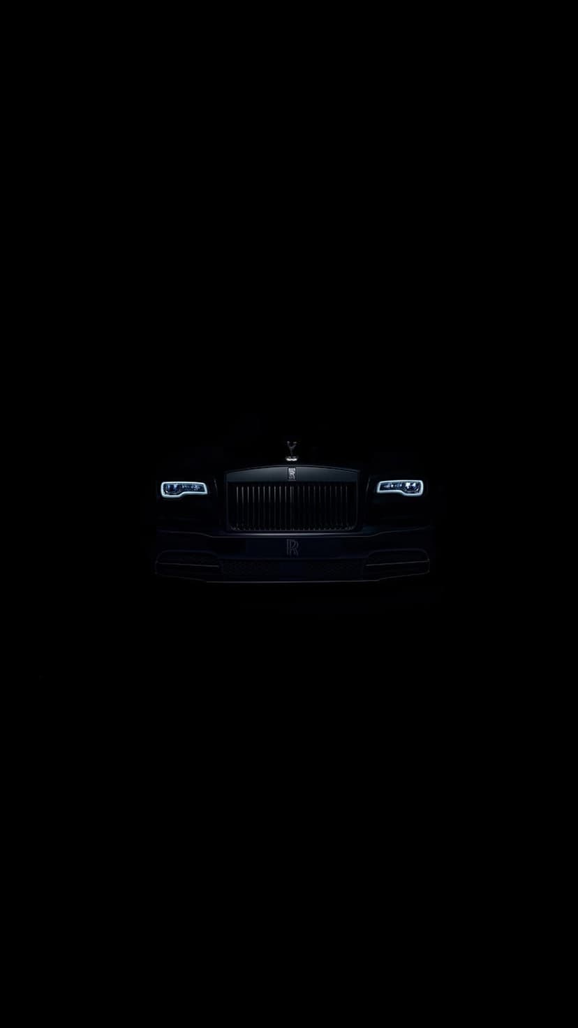 Black Rolls-Royce Phantom front grille and LED headlights with the Spirit of Ecstasy ornament in low light.