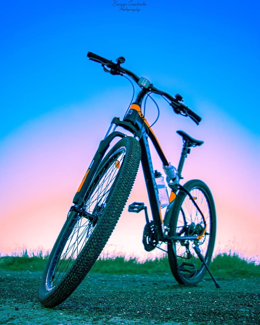 Black and orange mountain bike on a gravel path against a gradient blue and pink sunset sky at a low angle.