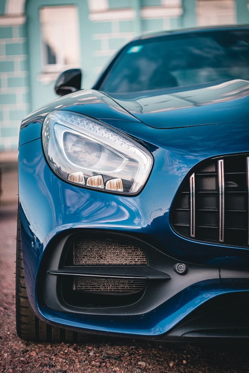 Metallic blue sports car front featuring LED headlights and a vertical chrome grille against a light building.