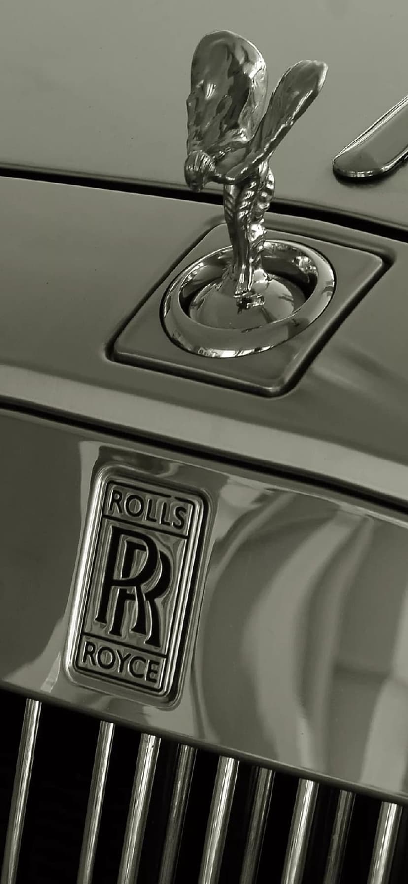 Spirit of Ecstasy figurine stands on a polished chrome grille with the Rolls-Royce emblem in monochrome.
