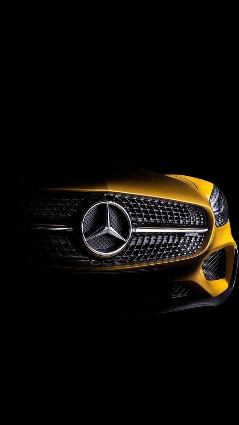 Gold Mercedes-Benz three-pointed star logo and black mesh grille illuminated by dramatic side lighting.