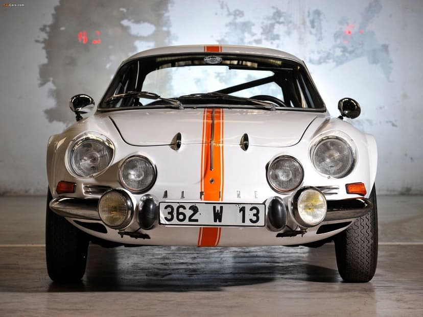 Front view of a white Alpine A110 classic rally car with orange racing stripes and multiple round headlights.