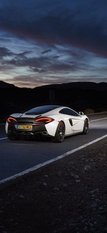 White McLaren 570S driving at sunset on a road