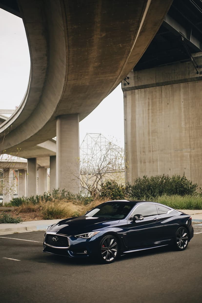 Infiniti Q60 coupe with red brake calipers parked under a curved concrete overpass on an urban asphalt road.