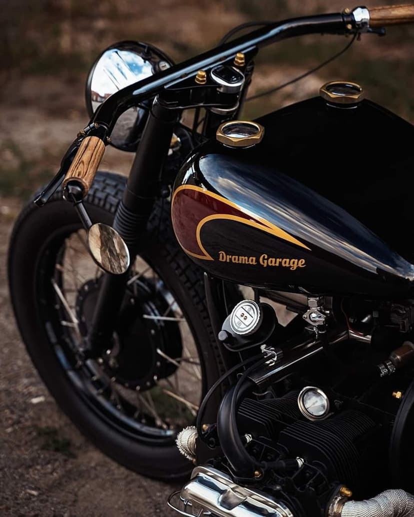 Vintage motorcycle with a glossy black gas tank, gold lettering, wooden grips, and a chrome headlight detail.