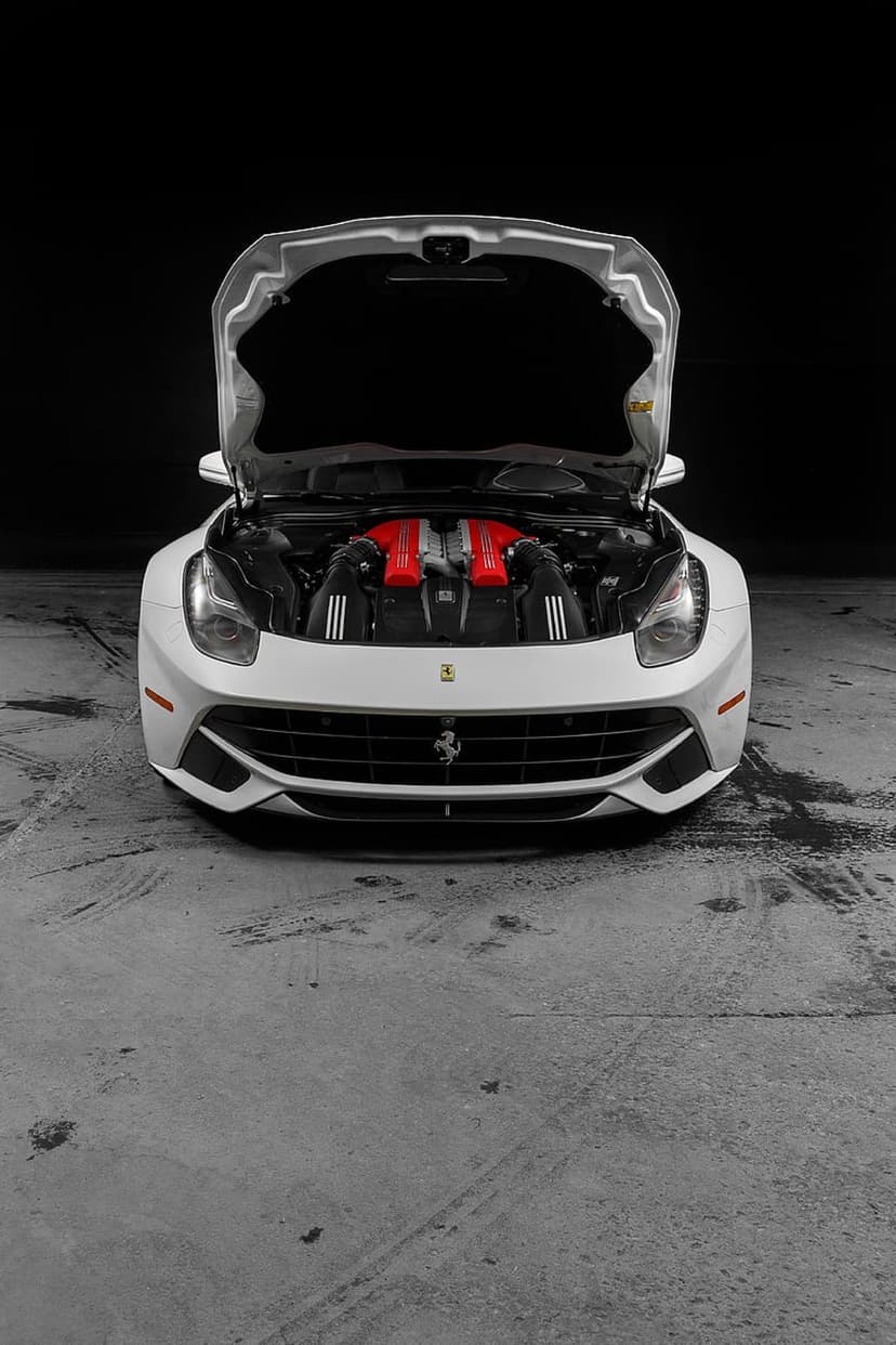 White Ferrari F12 with an open hood reveals vibrant red engine covers against a dark minimalist background.