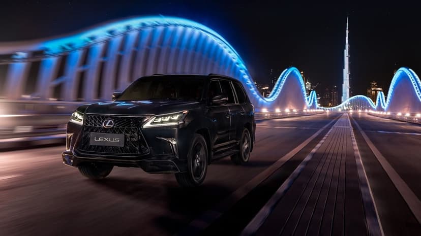 Black Lexus SUV driving on a bridge with glowing blue neon arches and Burj Khalifa in the night background.