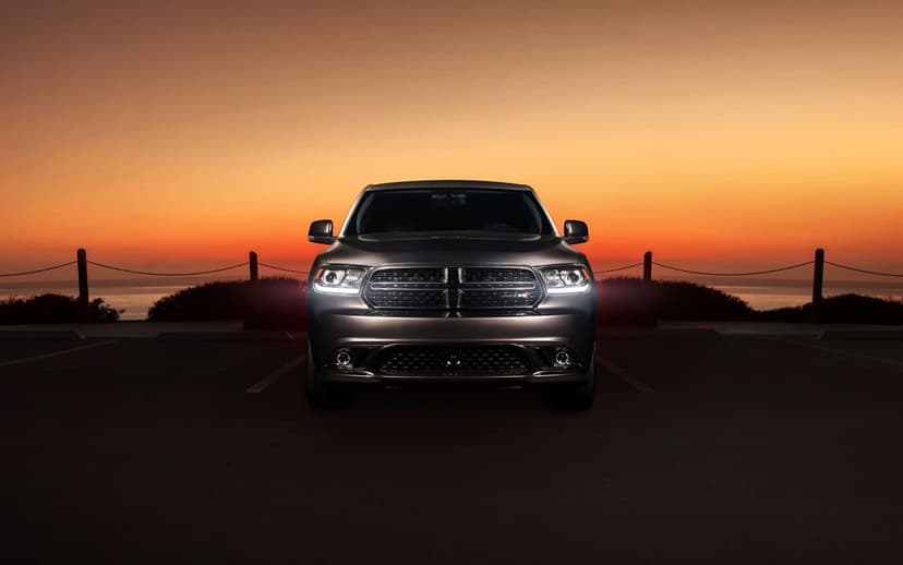 Front view of a Dodge Durango with glowing headlights parked against a vibrant orange sunset sky over the ocean.