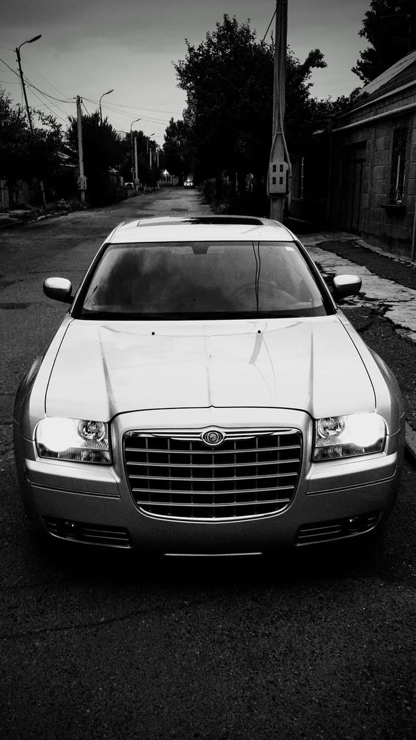 Chrysler 300 sedan parked on a city street with bare trees and streetlamps in a high-contrast black and white style.