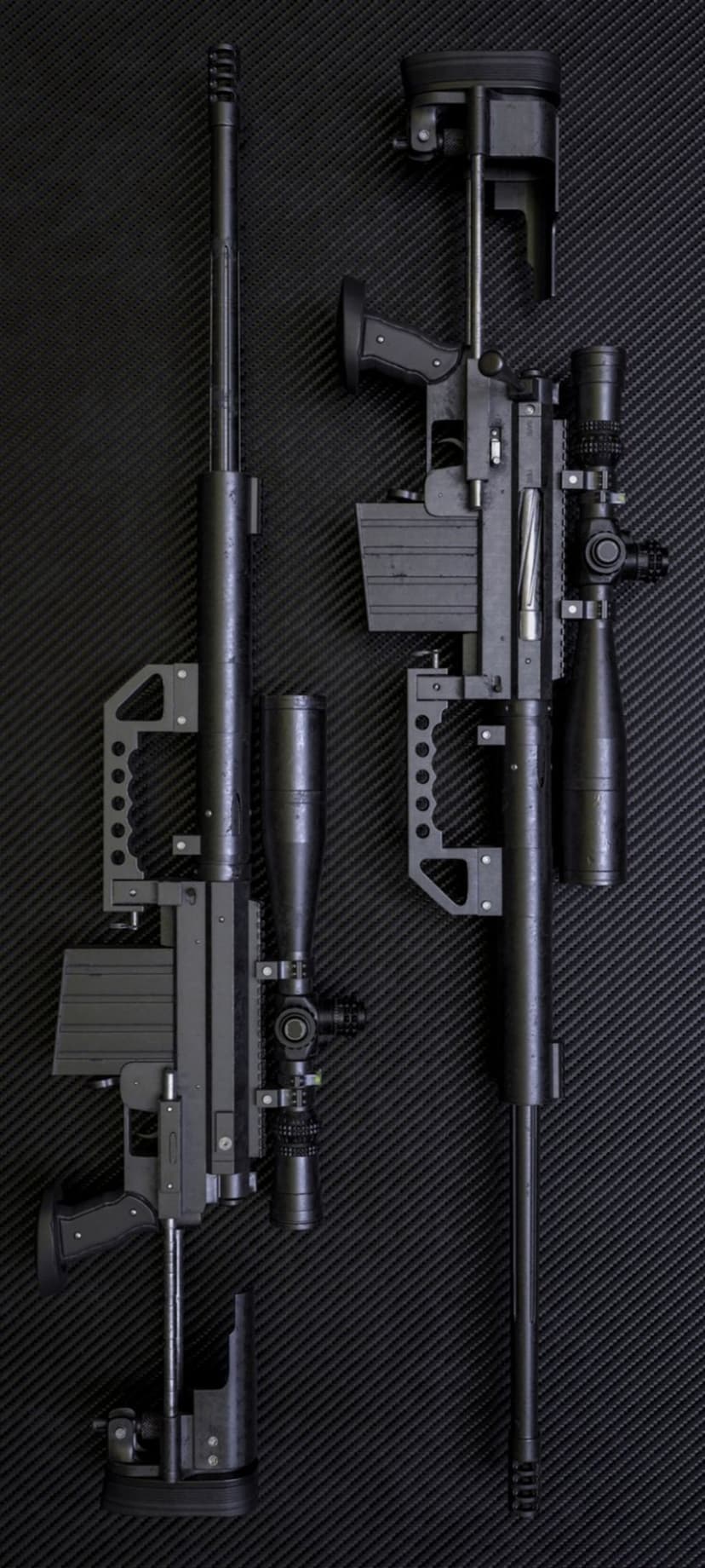 Pair of black tactical sniper rifles with telescopic scopes laid flat on a dark textured charcoal surface.