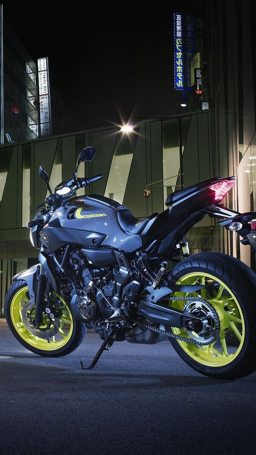 Yamaha MT-07 motorcycle with neon yellow rims parked on night asphalt near a glowing Japanese neon sign.