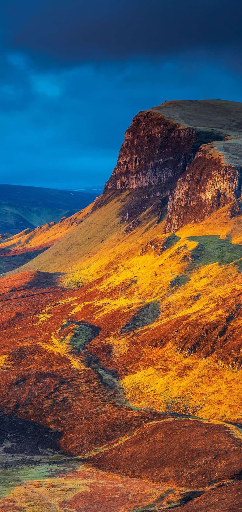 Rugged mountain peak glowing with orange sunset light beneath a deep blue twilight sky in a vertical landscape.