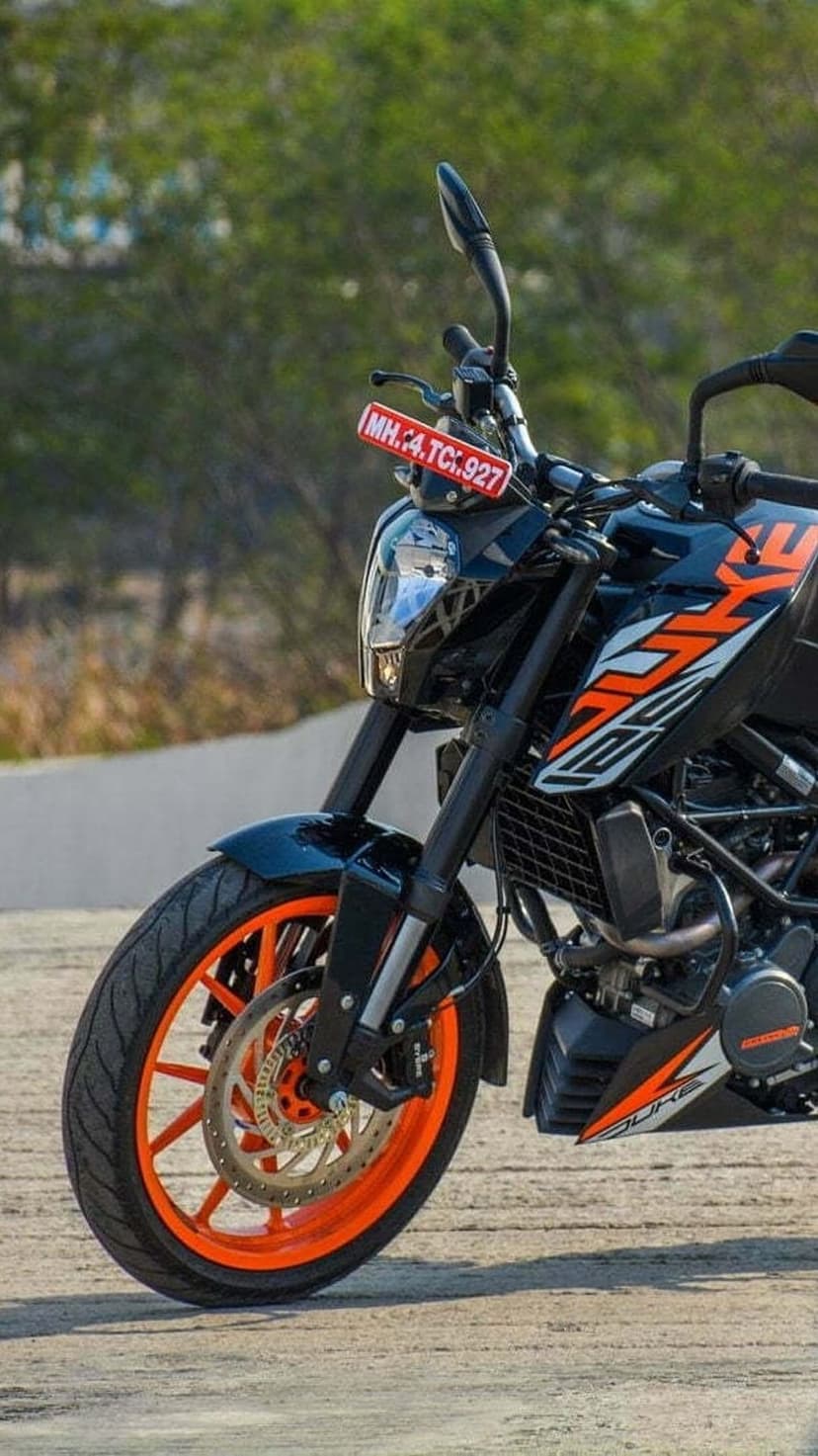 KTM Duke motorcycle with neon orange wheels and a red license plate parked on a gravel surface outdoors.