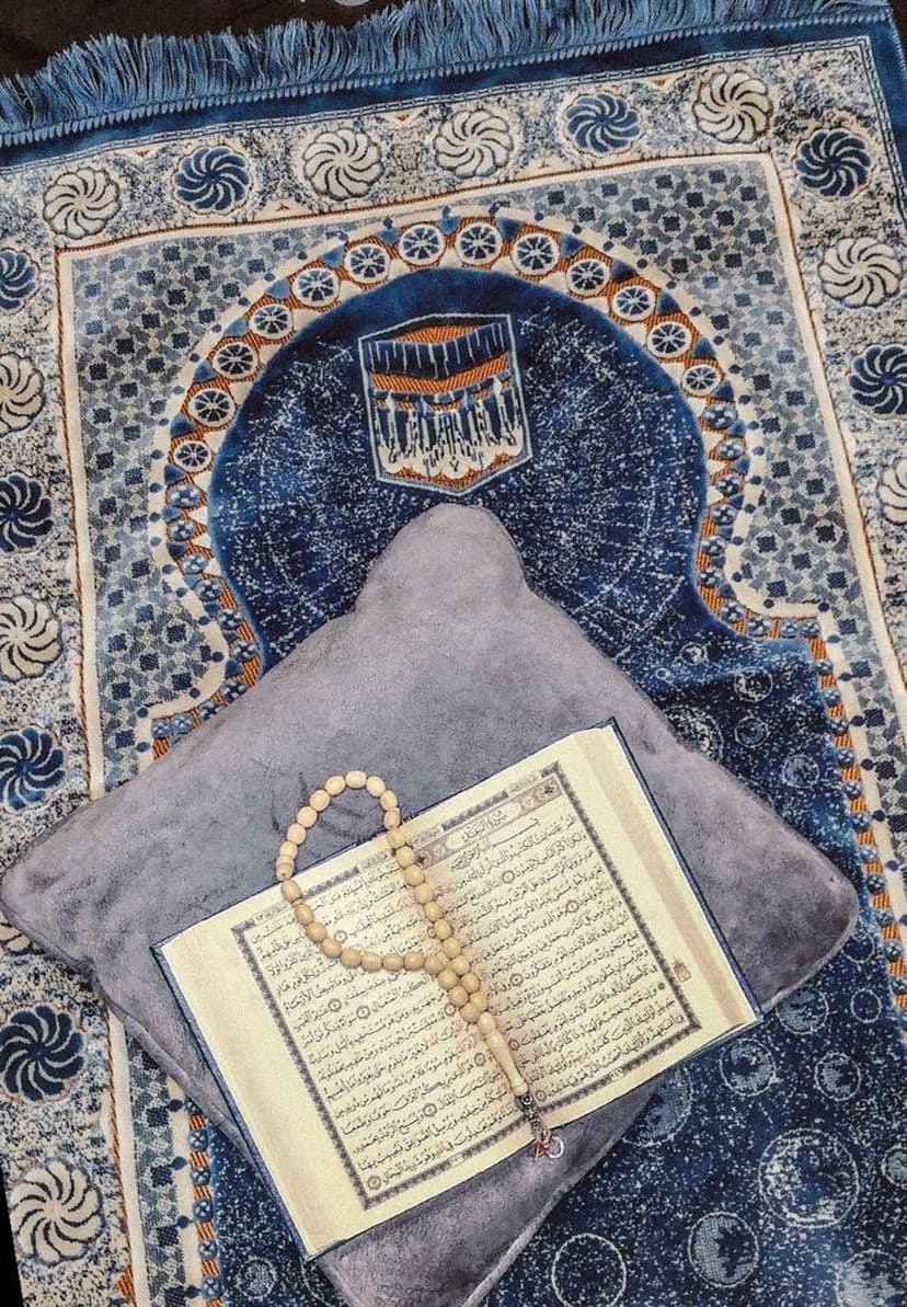 Open Quran with Arabic calligraphy, wooden prayer beads, and an ornate rug shown in a vertical close-up view.