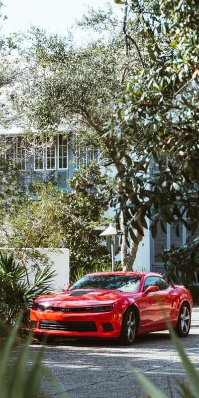Red Camaro parked by modern house with lush greenery