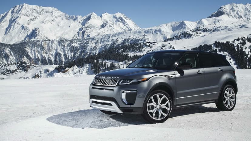 Gray Range Rover Evoque parked on a snowy field with massive snow-covered mountains in the background.