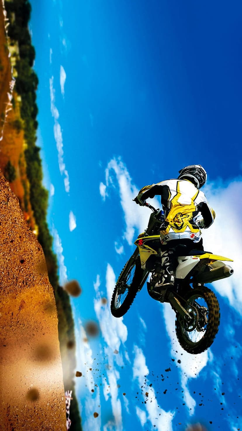 Motocross rider performs a high-altitude jump on a dirt bike against a blue sky with scattered white clouds.