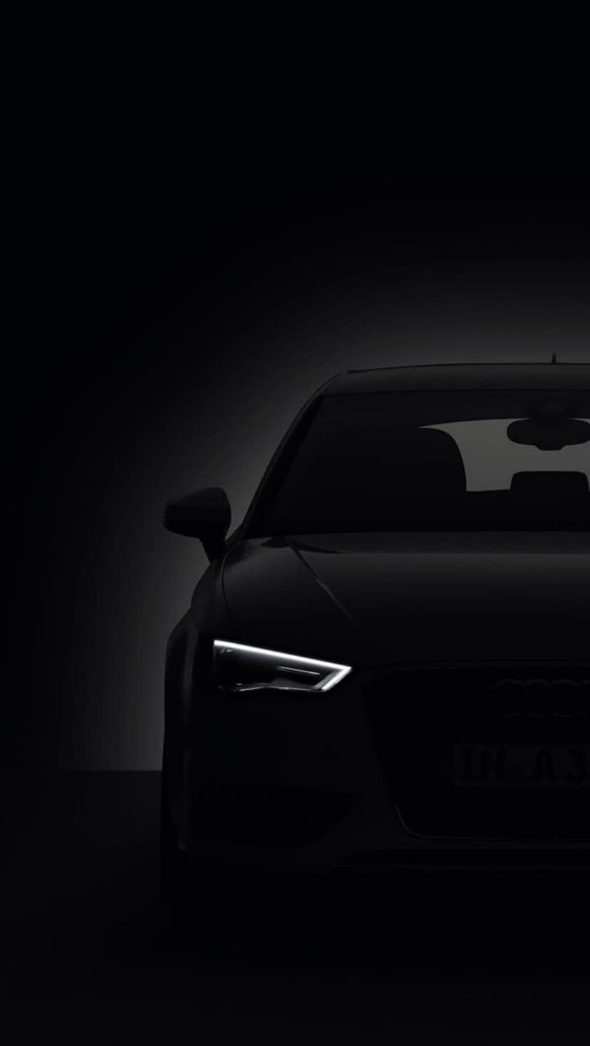 Black Audi A3 headlight glows with sharp white LED light against a dark car body and illuminated license plate.