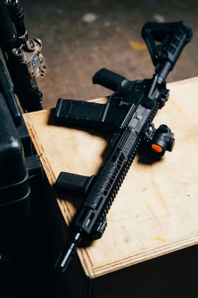 Modern tactical rifle with red dot sight on wooden surface