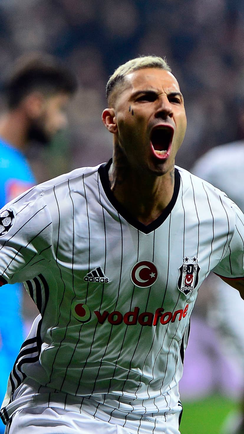 Footballer in a black and white striped jersey shouts with eyes closed during a goal celebration on the pitch.