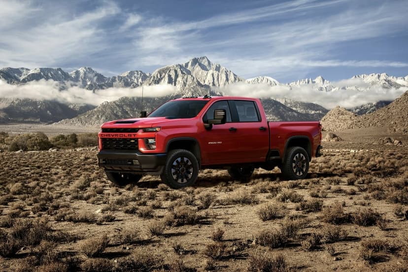 Red Chevrolet 2500 HD truck parked in a desert with snow-capped mountains and clouds in the background.