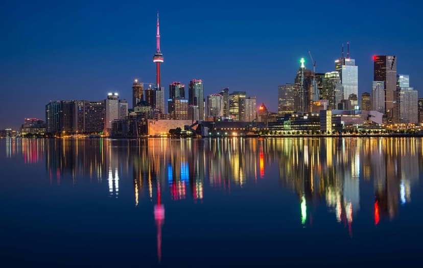 CN Tower and Toronto skyscrapers glowing at night with vibrant light reflections on calm harbor water.