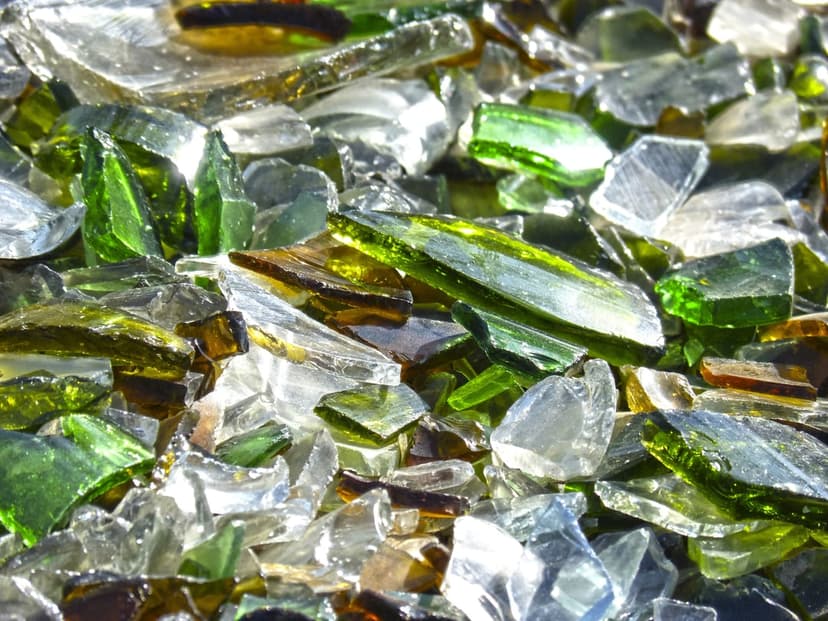 Sharp emerald, amber, and clear glass shards piled together with light reflecting off their jagged, translucent edges.