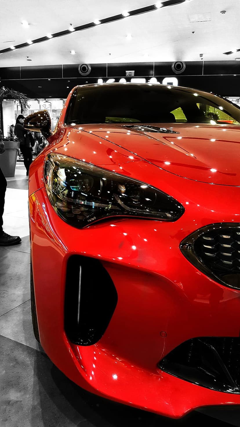 Red Kia Stinger front fascia showing detailed LED headlights, dark textured grille, and vibrant metallic paintwork.