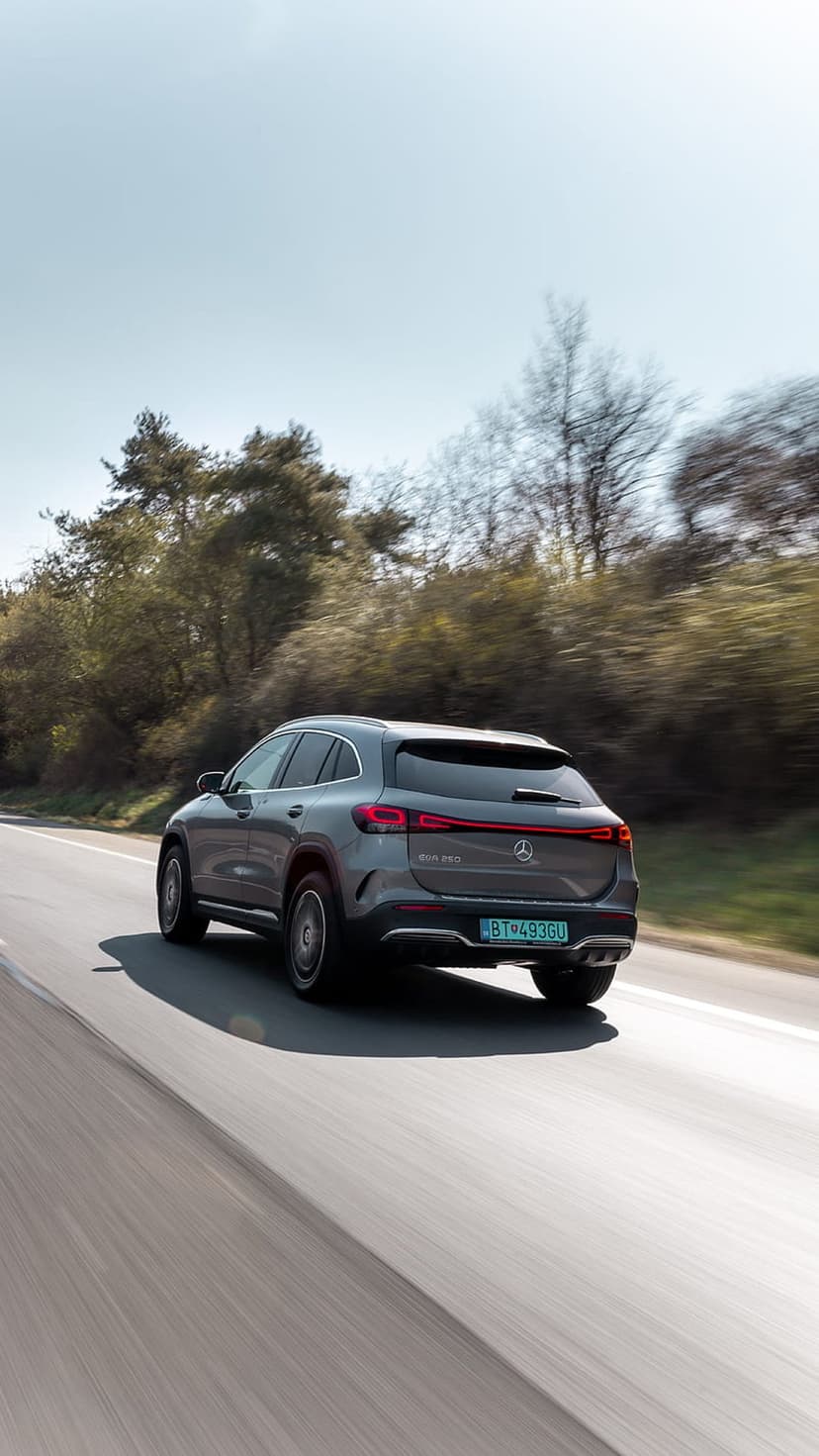 Gray Mercedes-Benz EQA electric SUV driving on a tree-lined road with glowing red taillights and motion blur.