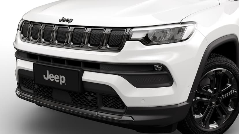 Front view of a white Jeep SUV showing the black seven-slot grille, LED headlight, and dark alloy wheels.