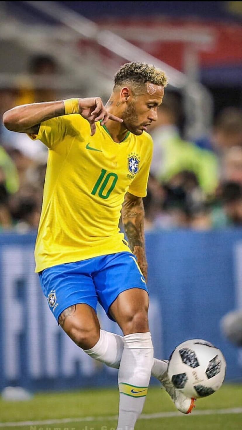Neymar Jr. controls a soccer ball while wearing a yellow Brazil jersey and blue shorts on a stadium field.