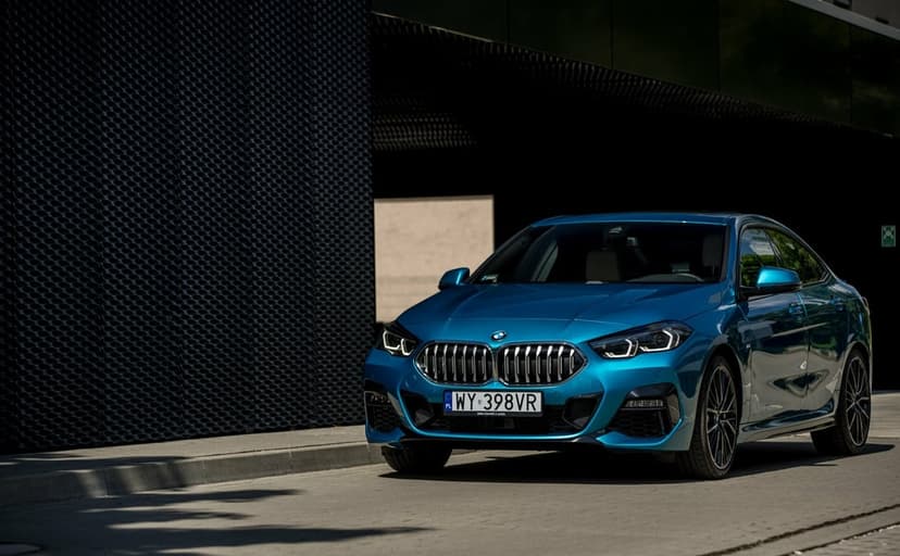 Blue BMW 2 Series Gran Coupe parked on a paved street against a dark, textured modern architectural wall.