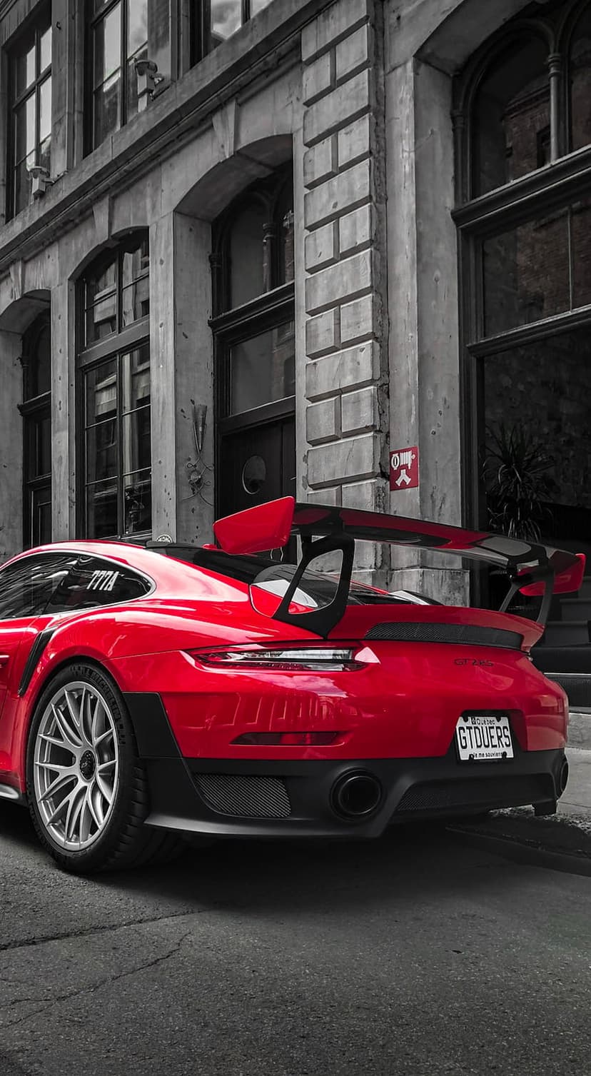 Red Porsche GT2 RS rear wing and taillights parked on a grayscale cobblestone street with stone buildings.
