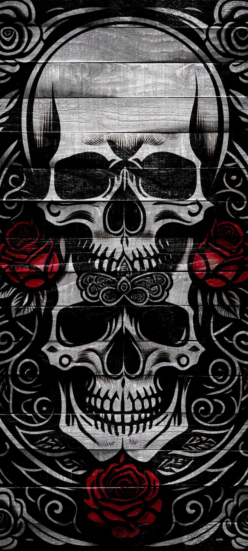 Two white skulls surrounded by red roses and black tribal patterns on a dark brown weathered wooden surface.