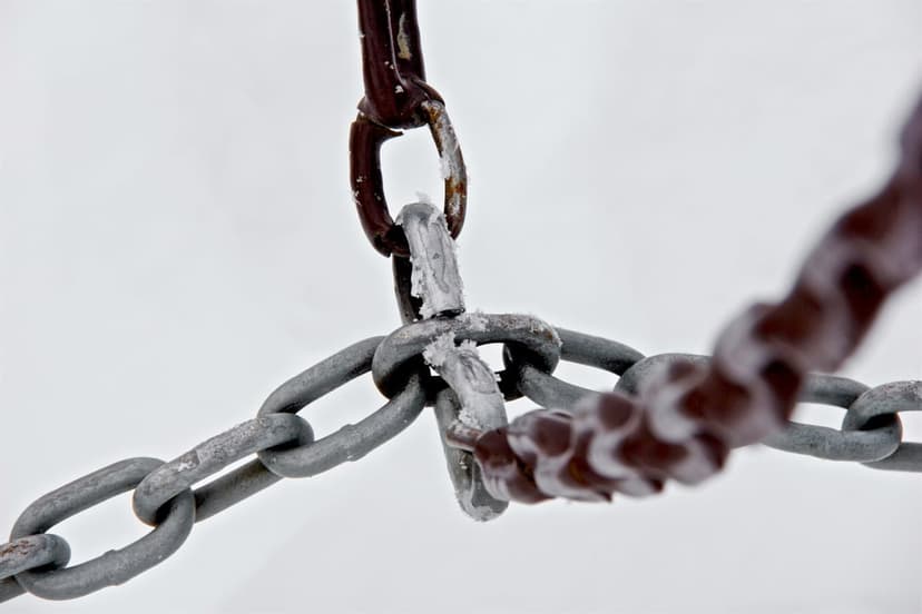 Metal chains covered in white frost and ice crystals against a bright, blurred backdrop in a macro composition.
