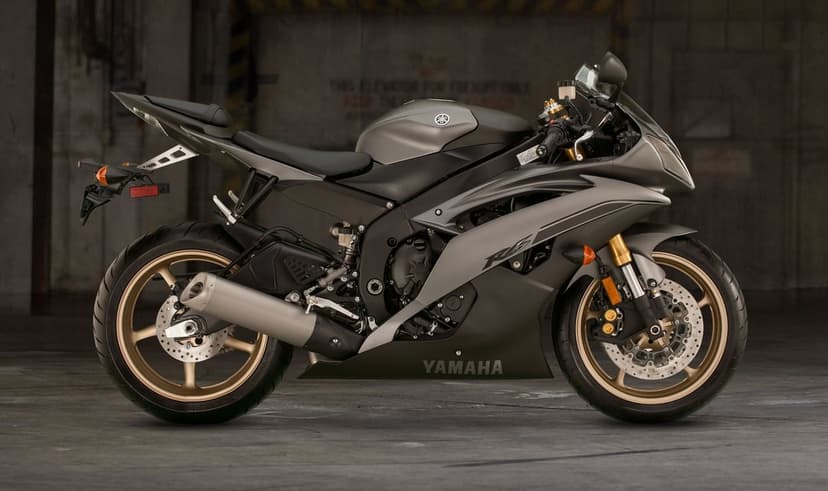 Side view of a matte grey Yamaha R6 motorcycle with gold wheels and forks in a dark industrial garage.