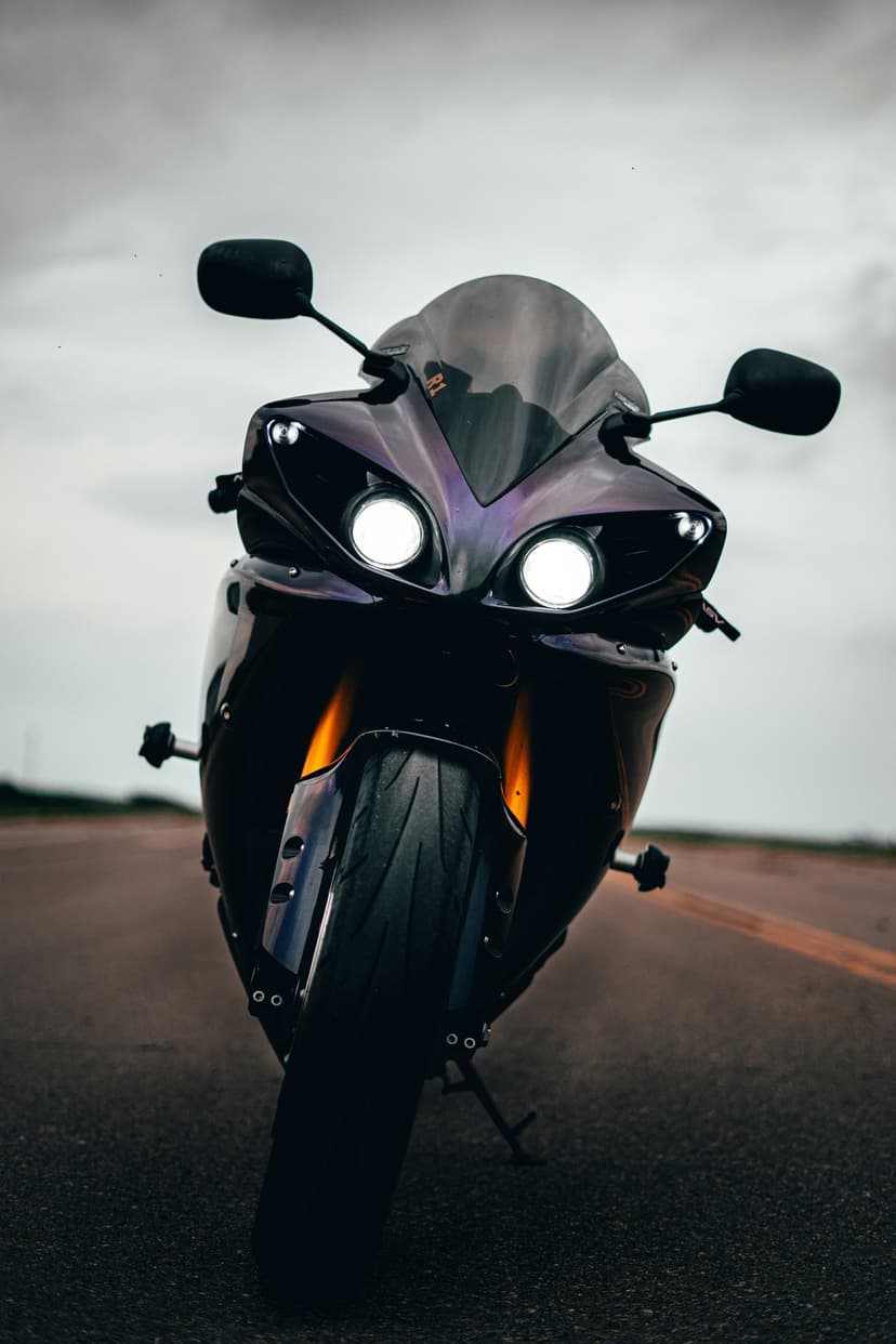 Black sport motorcycle with glowing white headlights parked on a gray asphalt road under an overcast sky.